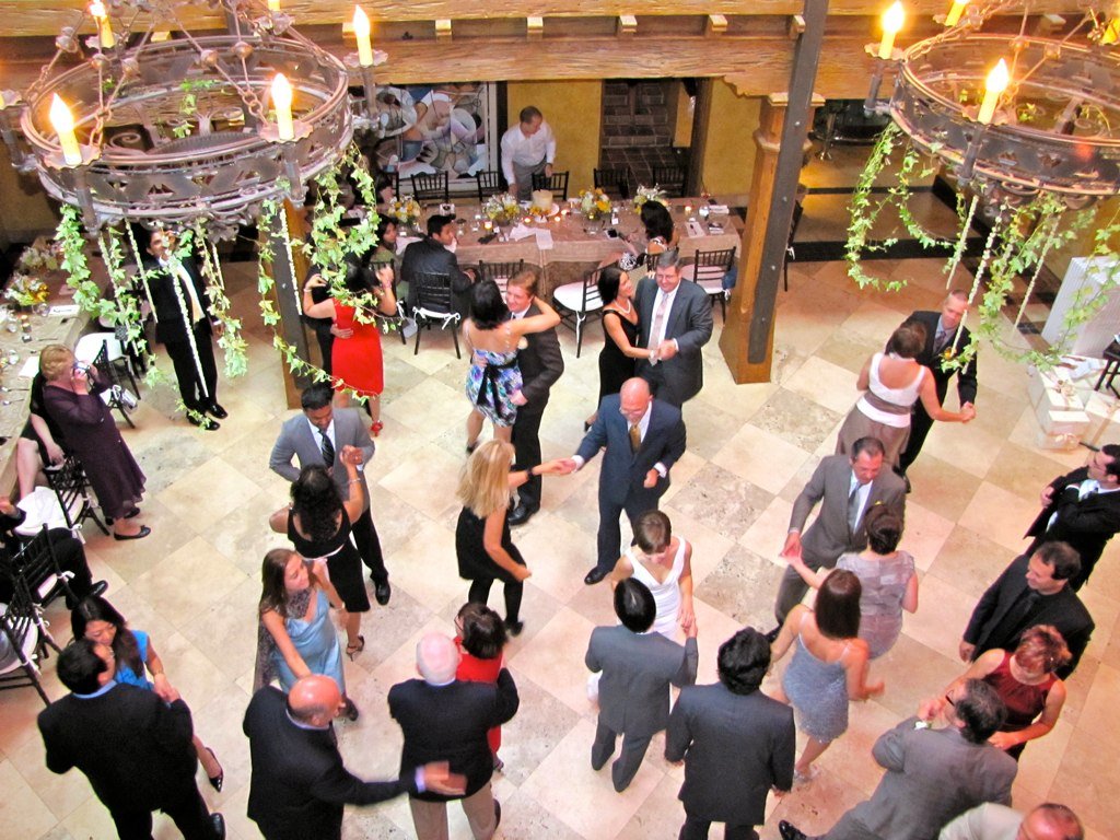 "A vibrant wedding dance floor filled with guests of all ages joyfully dancing under colorful lights, creating a lively and celebratory atmosphere."